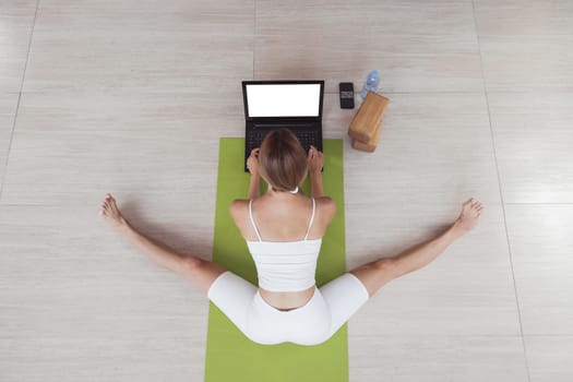 Young fit woman in sportswear doing sport or yoga online with laptop. Remote workouts, online trainer. Top view. Laptop with blank screen
