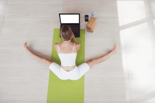 Young fit woman in sportswear doing sport or yoga online with laptop. Remote workouts, online trainer. Top view. Laptop with blank screen
