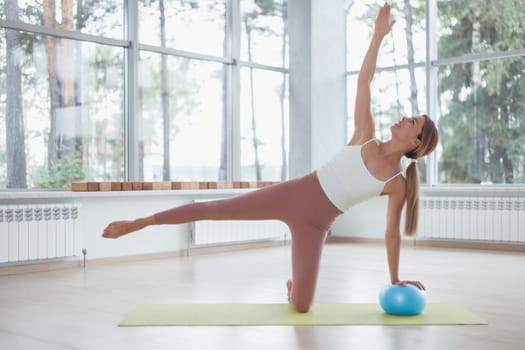 Young woman working out with a ball indoors on green mat.