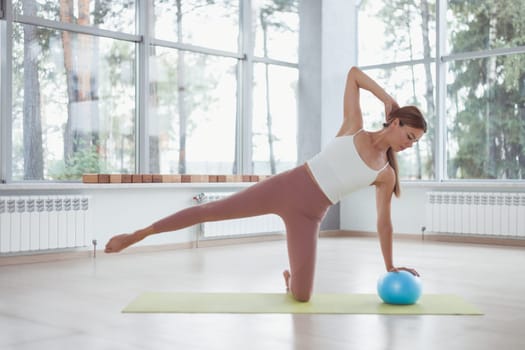 Young woman working out with a ball indoors on green mat.