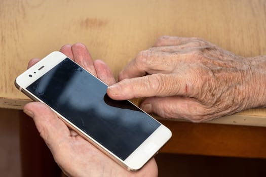 Elderly senior woman holding white mobile phone in her hands, closeup detail.