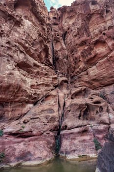 Tall red rocky wall with water on ground - Wadi Rum scenery.