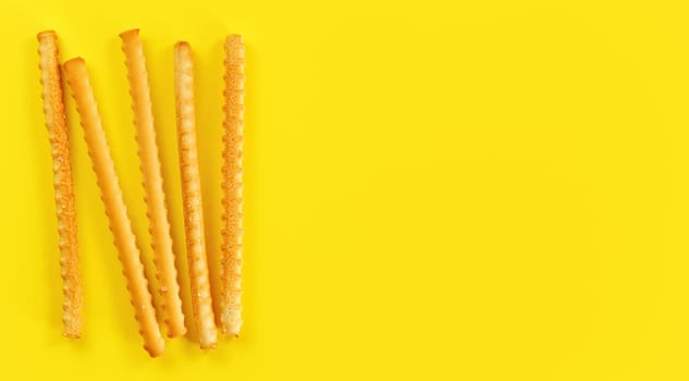Grissini, also known as breadsticks on yellow board, view from above space for text right side.