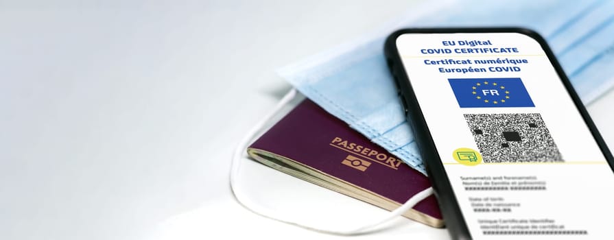 French EU Digital COVID Certificate with the QR code. Translation from french "European COVID digital certificate"". Mobile phone over a surgical mask and a french passport. Health passport. Copy space"