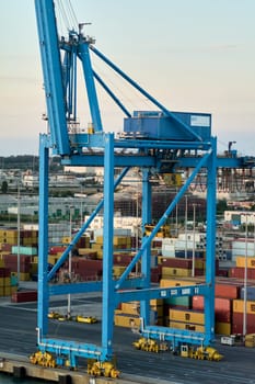 Civitavecchia. Italy - February 17, 2025: Impressive blue crane at Civitavecchia handling containers amidst a bustling shipping environment. Ideal for illustrating industrial and maritime activities.