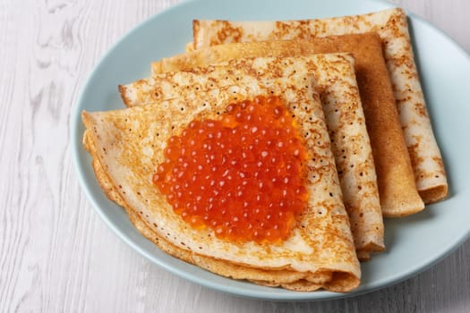 Savory crepes filled with fresh orange fish roe served on a light blue plate at a cozy breakfast table.