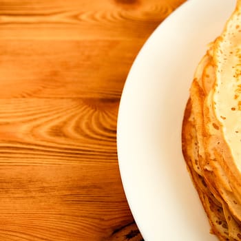 Pancakes on a plate on a wooden table. A large stack of fresh pancakes. Delicious healthy fresh pancakes. Place for advertising, logo, lettering, layout, mockup.