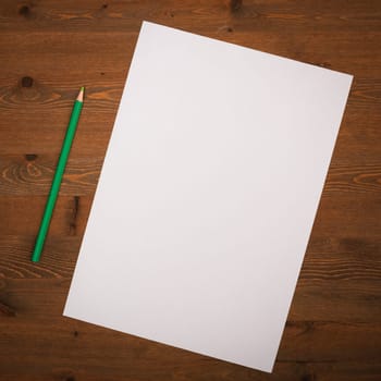A blank white sheet and pencil for drawing on a wooden background with space for copying and lettering. Layout, mockup free space.