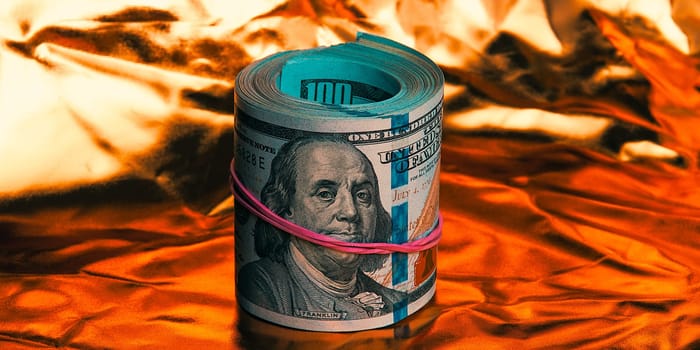 A roll of one hundred American dollars in close-up on a gold background. A big pile of cash dollars. One hundred dollar bills. Close-up, free space for captions and text.