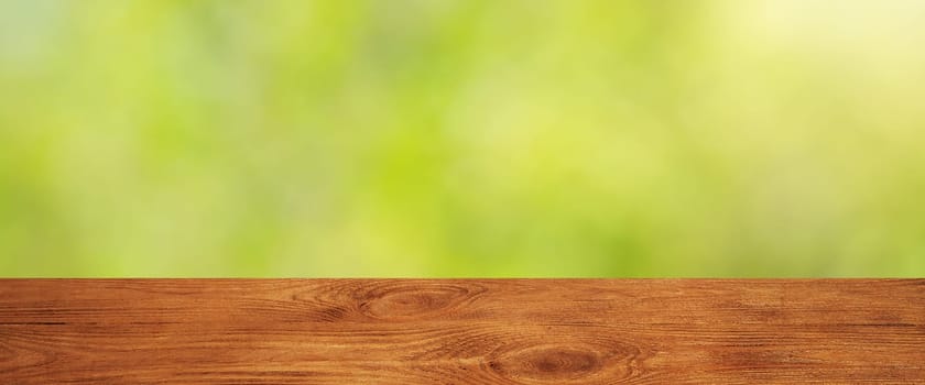 Background with blurred green leaves and empty wooden planks in the foreground. For product demonstrations, free space, layout, mockup, perspective board, background board.