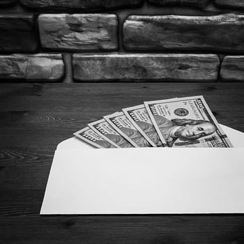 Dollars in one-hundred-dollar bills are spread out in an envelope on a table near the brick wall. Dollars fanned out. US dollars. On the envelope there is a place for an inscription, a logo. Black and white style. Layout, template, mockup.