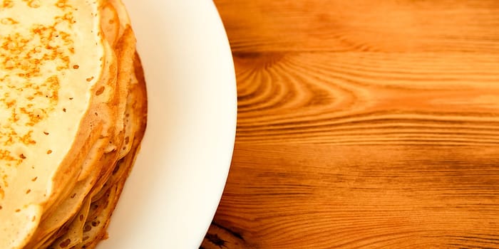 Pancakes on a plate on a wooden table. A large stack of fresh pancakes. Delicious healthy fresh pancakes. Place for advertising, logo, lettering, layout, mockup.