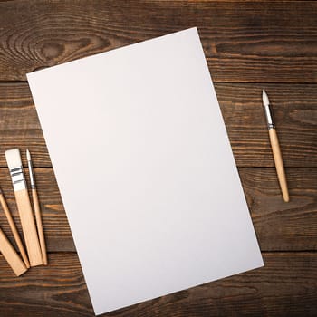 A clean white sheet and brushes on a textured background with space to copy. Layout, mockup space for text and drawing.