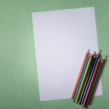 A blank white sheet and colored pencils for drawing on a plain textured background with space for copying and lettering. Layout, mockup free space.