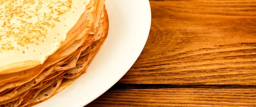 Pancakes on a plate on a wooden table. A large stack of fresh pancakes. Delicious healthy fresh pancakes. Place for advertising, logo, lettering, layout, mockup.