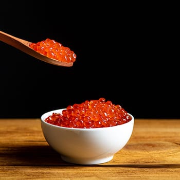 Red caviar in a wooden cup on a black background with a spoon. A large pile of bright caviar. Fresh delicious caviar. A place for advertising, logo, label, layout, mockup. Layout, template.