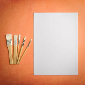 A clean white sheet and brushes on a textured background with space to copy. Layout, mockup space for text and drawing.