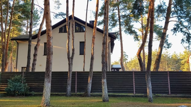 Large stylish and modern residential building and a huge courtyard with trees and flowers in a forest with sunbeams