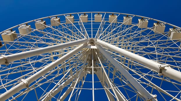 Big white ferris wheel against the blue sky. Part of the attraction on a blue background with copy space. Cabins, viewing platforms