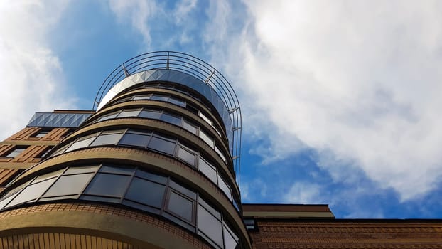 Ukraine, Kiev - August 20, 2019: A tall brown building with windows in the sun and shadow under a blue sky and white clouds. Photo taken from bottom to top