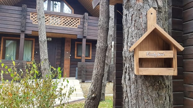 Beautiful birdhouse made of wood in the forest near a brown country wooden house. Homemade bird feeder. Art birdhouse on a tree in the garden
