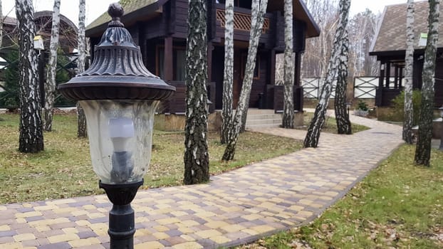 Night illumination of walking paths on the street for walks in a country hotel with wooden houses in the forest. Small retro-style solar lamp with motion sensors in the courtyard of the townhouse.