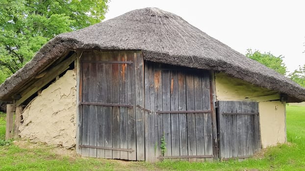 Ukraine, Kiev - June 11, 2020. Old peasant Ukrainian house or barn in the summer with a thatched roof in the village. Pirogovo Museum in the open air of different regions of Ukraine