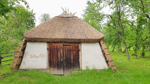 Ukraine, Kiev - June 11, 2020. Old peasant Ukrainian house or barn in the summer with a thatched roof in the village. Pirogovo Museum in the open air of different regions of Ukraine
