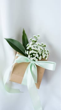 The gift comes in minimalist packaging, decorated with a neutral, calm blue ribbon and flowers symbolizing the arrival of spring. High quality photo