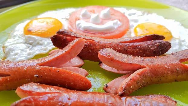 Top view of fried egg and sausages on a green plate, serving breakfast for the baby.
