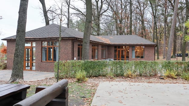 Ukraine, Bucha - October 20, 2019: a large stylish house made of brown stone, large windows and a huge courtyard with trees. Beautiful brick house in the autumn forest. European village house