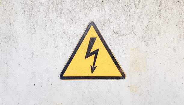 Danger sign of high voltage electricity. Yellow triangular sign with a lightning in the center. This warning is written on an old metal surface painted with gray paint