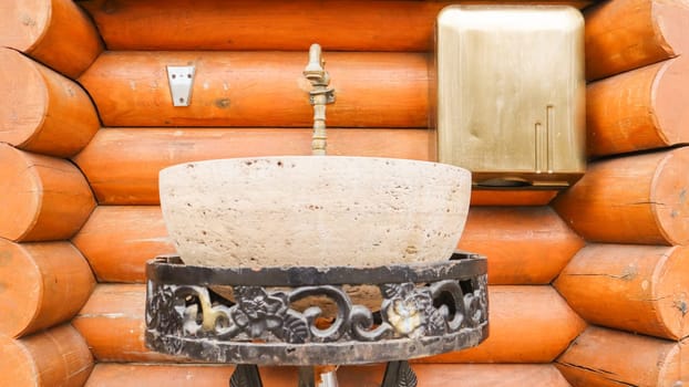 A stone washbasin on a metal forged stand in a log house. Interior in a house made of wood