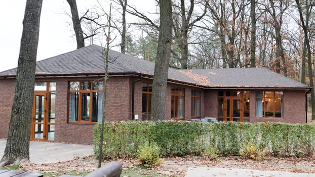 Ukraine, Bucha - October 20, 2019: a large stylish house made of brown stone, large windows and a huge courtyard with trees. Beautiful brick house in the autumn forest. European village house