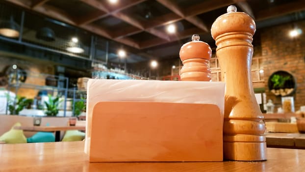 Ukraine, Kiev - September 1, 2019: A table in a cafe or restaurant. White napkins in a wooden napkin holder, spices salt and pepper on a wooden table, panoramic view.