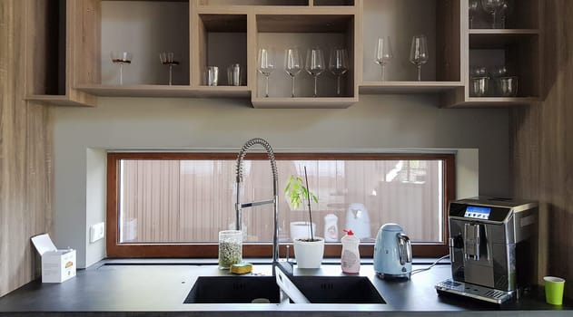 Ukraine, Kiev - September 24, 2019: Modern kitchen with brown wooden furniture, stone countertops, sink and faucet. A coffee machine is on the table. Interior, kitchen design in a big house. Kitchen worktop and kitchen area