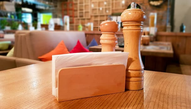 Ukraine, Kiev - September 1, 2019: A table in a cafe or restaurant. White napkins in a wooden napkin holder, spices salt and pepper on a wooden table, panoramic view.