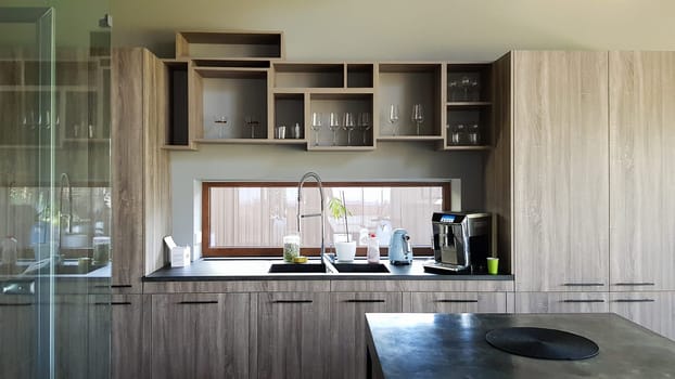 Ukraine, Kiev - September 24, 2019: Modern kitchen with brown wooden furniture, stone countertops, sink and faucet. A coffee machine is on the table. Interior, kitchen design in a big house. Kitchen worktop and kitchen area