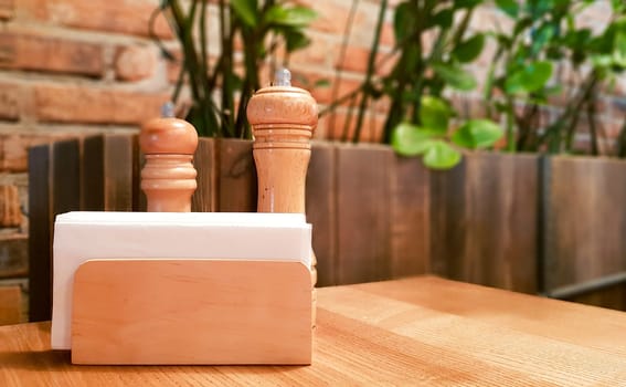 Ukraine, Kiev - September 1, 2019: A table in a cafe or restaurant. White napkins in a wooden napkin holder, spices salt and pepper on a wooden table, panoramic view.