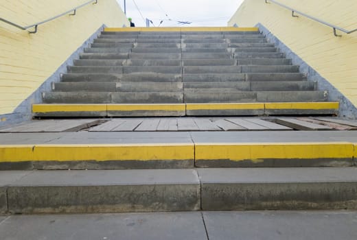 Empty yellow underground pedestrian crossing. Tunnel and daylight at the end. Steps to the top at the pedestrian crossing. A long concrete tunnel with lanterns in the city underground