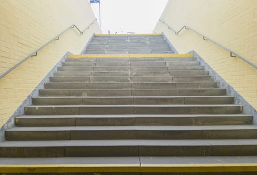 Empty yellow underground pedestrian crossing. Tunnel and daylight at the end. Steps to the top at the pedestrian crossing. A long concrete tunnel with lanterns in the city underground