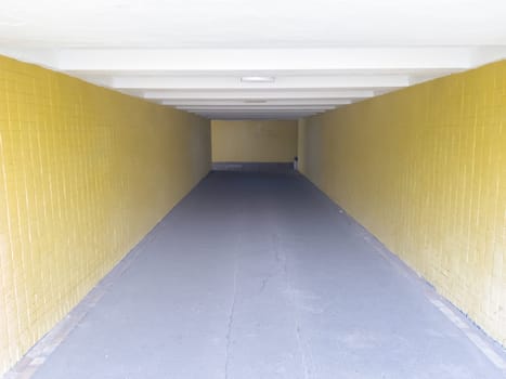 Empty yellow underground pedestrian crossing. Tunnel and daylight at the end. Steps to the top at the pedestrian crossing. A long concrete tunnel with lanterns in the city underground