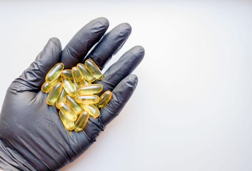 fish oil capsules in hand in a black medical glove on a white background, the hand takes one tablet from a saucer or plate. Hand holding omega 3 capsule on a white background. Healthcare concept.