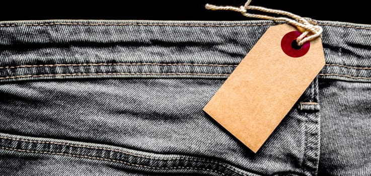 Closeup jeans with blank cardboard white price tag for your text. Tag the white mockup on the blue jeans. Empty copy space. Background, holiday concept. Black Friday - International Day of Shopping, Promotions, Discounts, Sales. Sales season is the fourth Thursday of November. Copy space, place for text, flat lay.