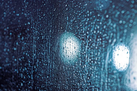 Close up of rain drops on the window in rainy night, cool lights