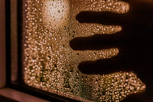 Close up of hand silhouette on window with water drops, night