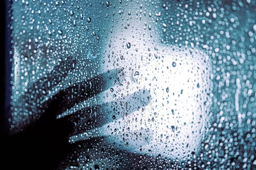 Close up of hand silhouette on window with water drops, night