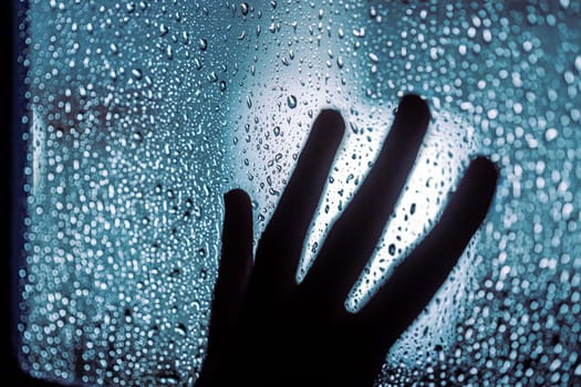 Close up of hand silhouette on window with water drops, night