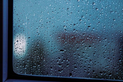 Close up of rain drops on the window in rainy night, cool lights and window frame
