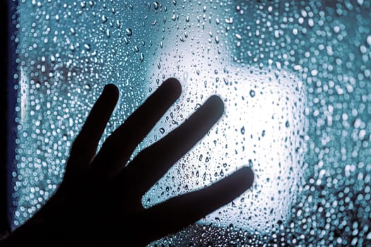 Close up of hand silhouette on window with water drops, night